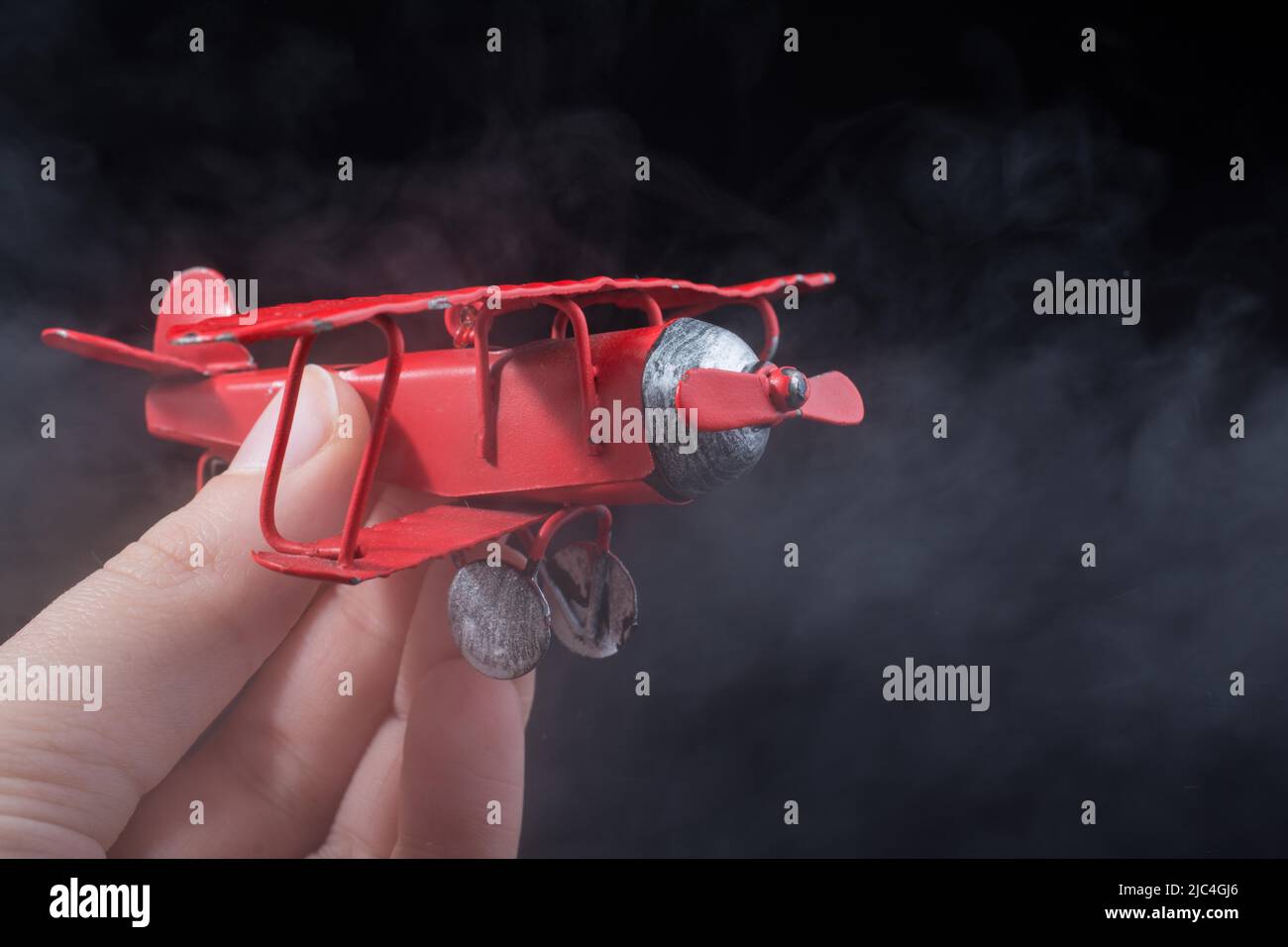 Hand holding a red toy plane on a black background Stock Photo