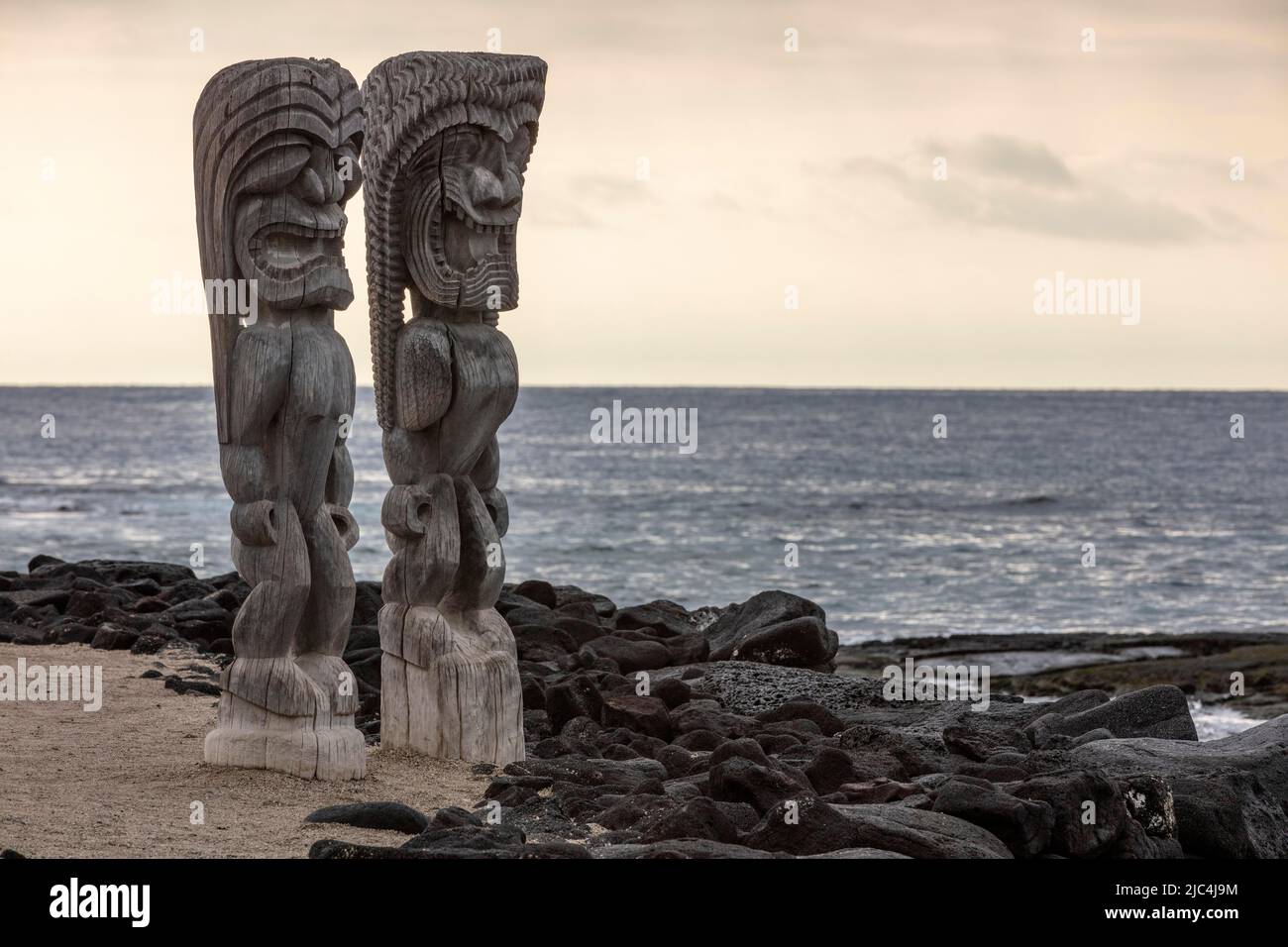 Wooden guardian figure, tiki in front of wall of lava stones and the