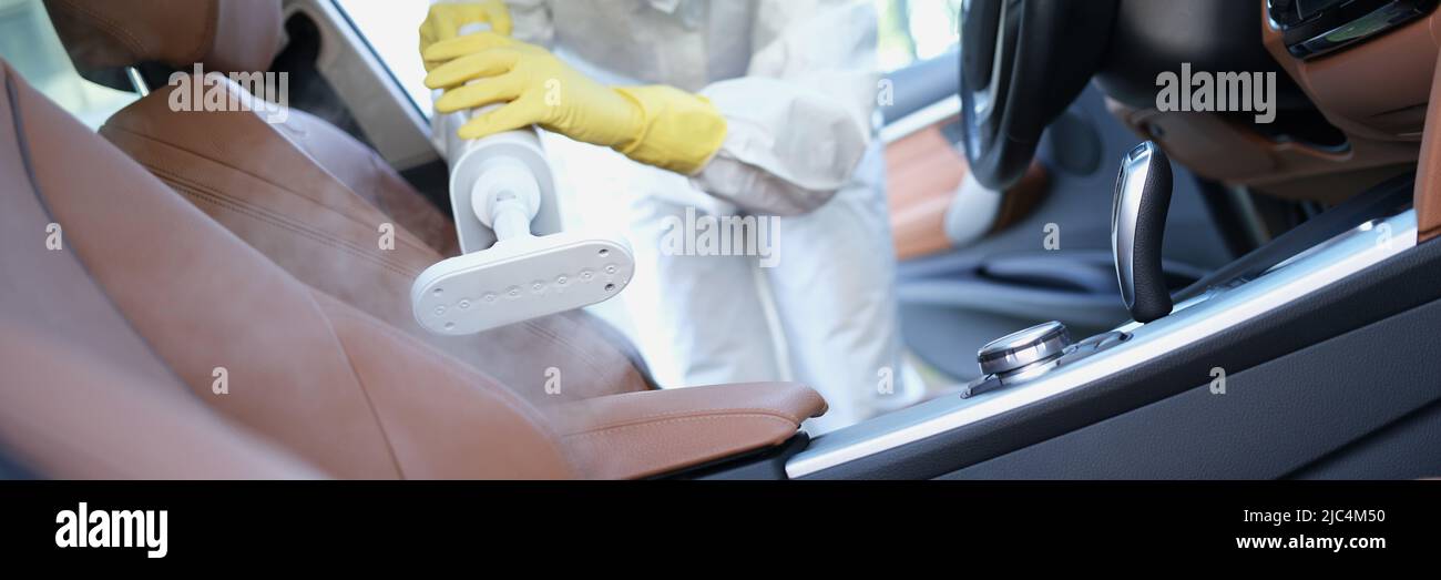 Hazmat worker cleansing car interior with spray disinfectant and steam