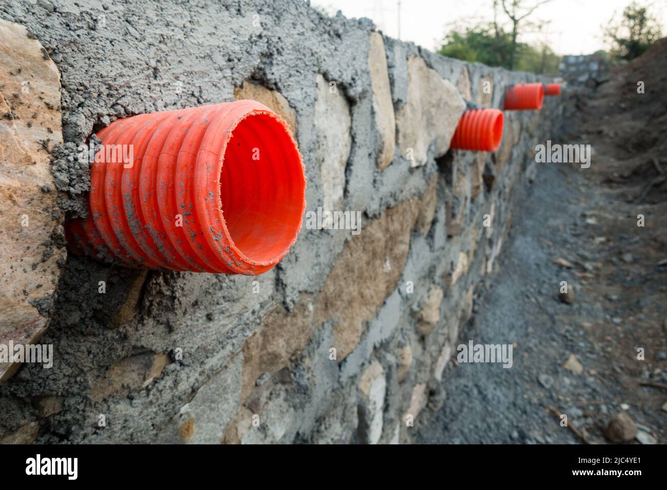 A row of orange culverts or water outlet pipes through a stone retaining wall for storm drainage in the hills of Uttarakhand India. Stock Photo