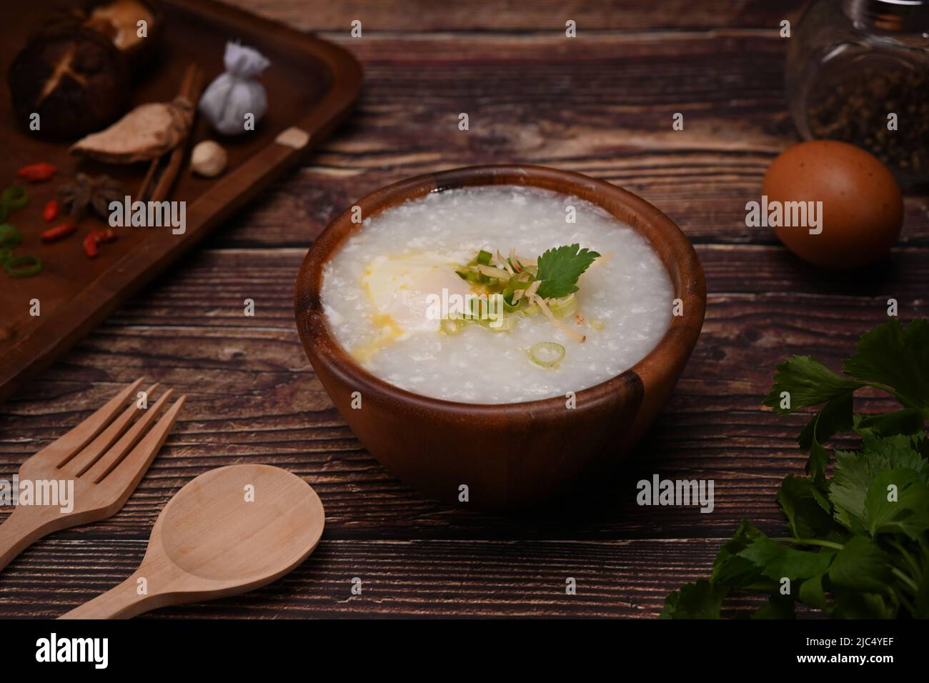 Testy rice porridge with soft boiled egg, and spring onion in wooden bowl for healthy breakfast Stock Photo