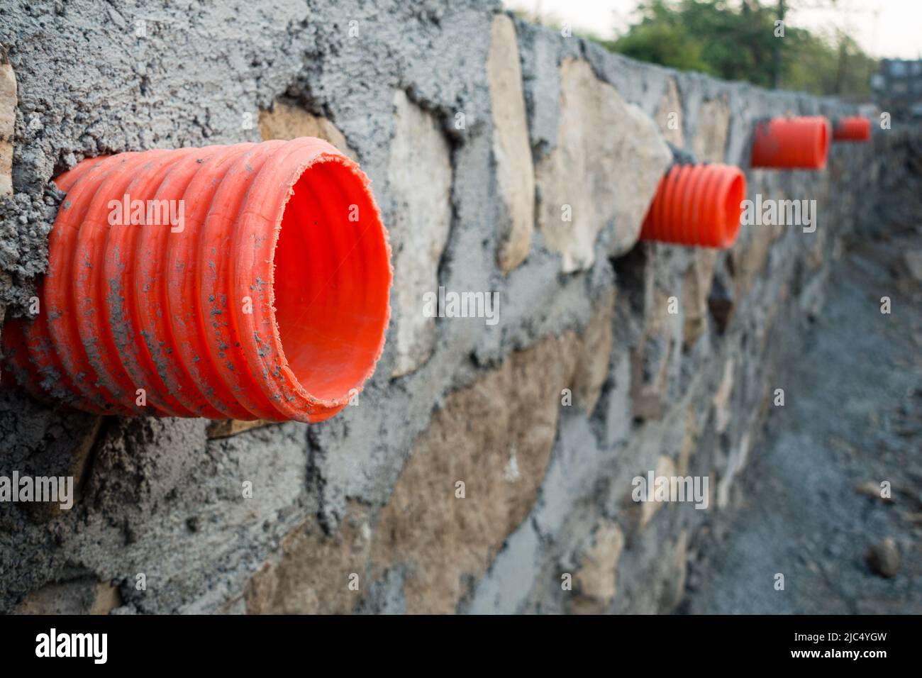 A row of orange culverts or water outlet pipes through a stone retaining wall for storm drainage in the hills of Uttarakhand India. Stock Photo