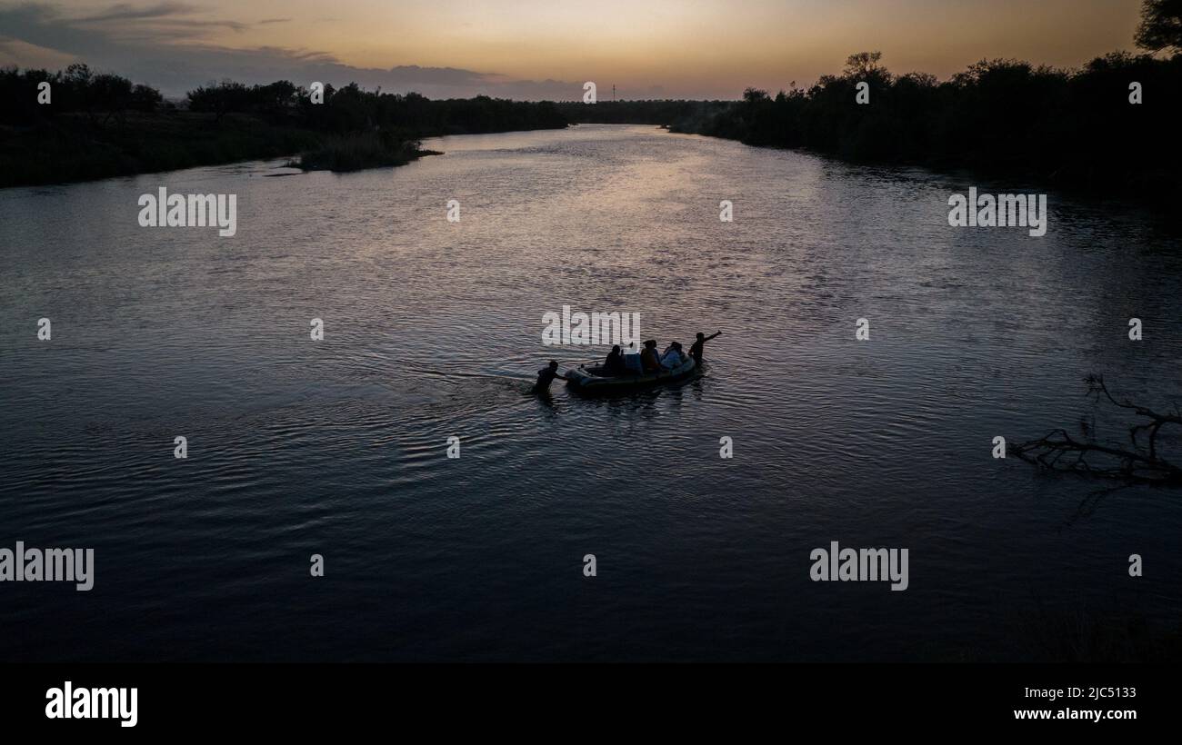 A smuggler signs towards another as he pulls a raft full of asylum seeking migrants from Central and South America across the Rio Grande river into Roma, Texas, U.S., June 9, 2022. Picture taken June 9, 2022. Picture taken with a drone.  REUTERS/Adrees Latif Stock Photo