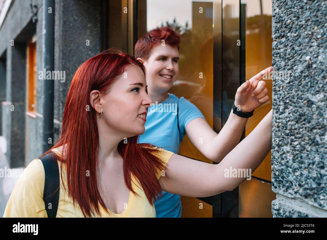 two young, urban woman ringing the doorbell of a block of buildings in a big city. young girls in the city sharing free time while gossiping. concept Stock Photo