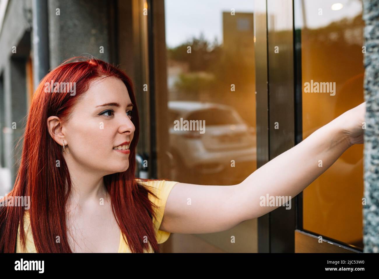 young woman smiling, ringing the doorbell of a friend's house in a block of buildings in a big city. girl stops by to pick up her friend. concept of Stock Photo