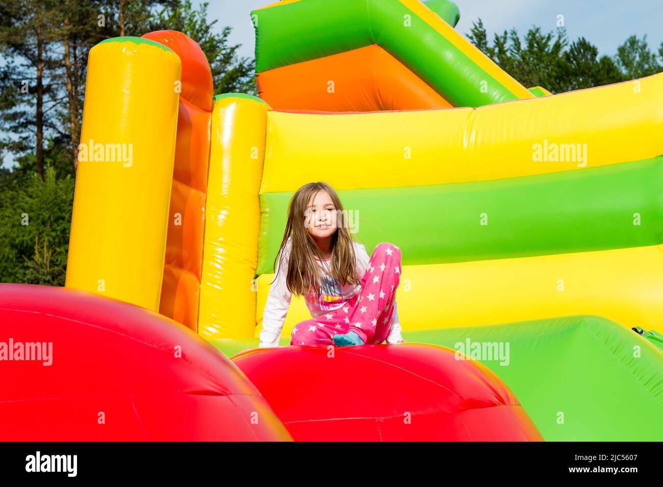 Happy little girl on a jumping castle, resting, during jumping from ball to ball on sunny day. Stock Photo