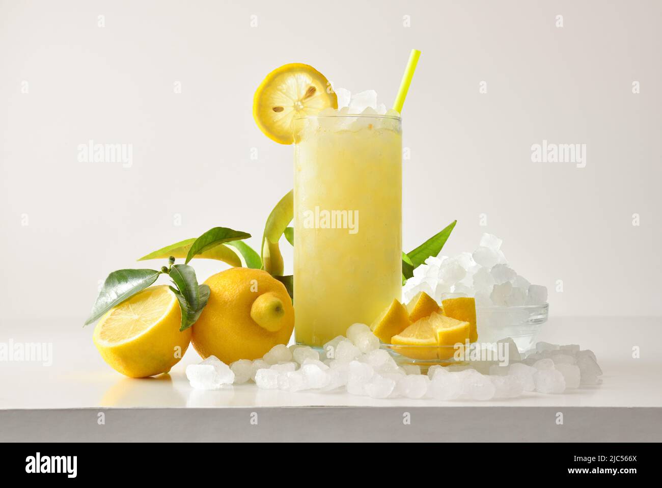 Lemon slush in tall glass with fruit and crushed ice around it on white table with isolated background. Front view. Horizontal composition. Stock Photo
