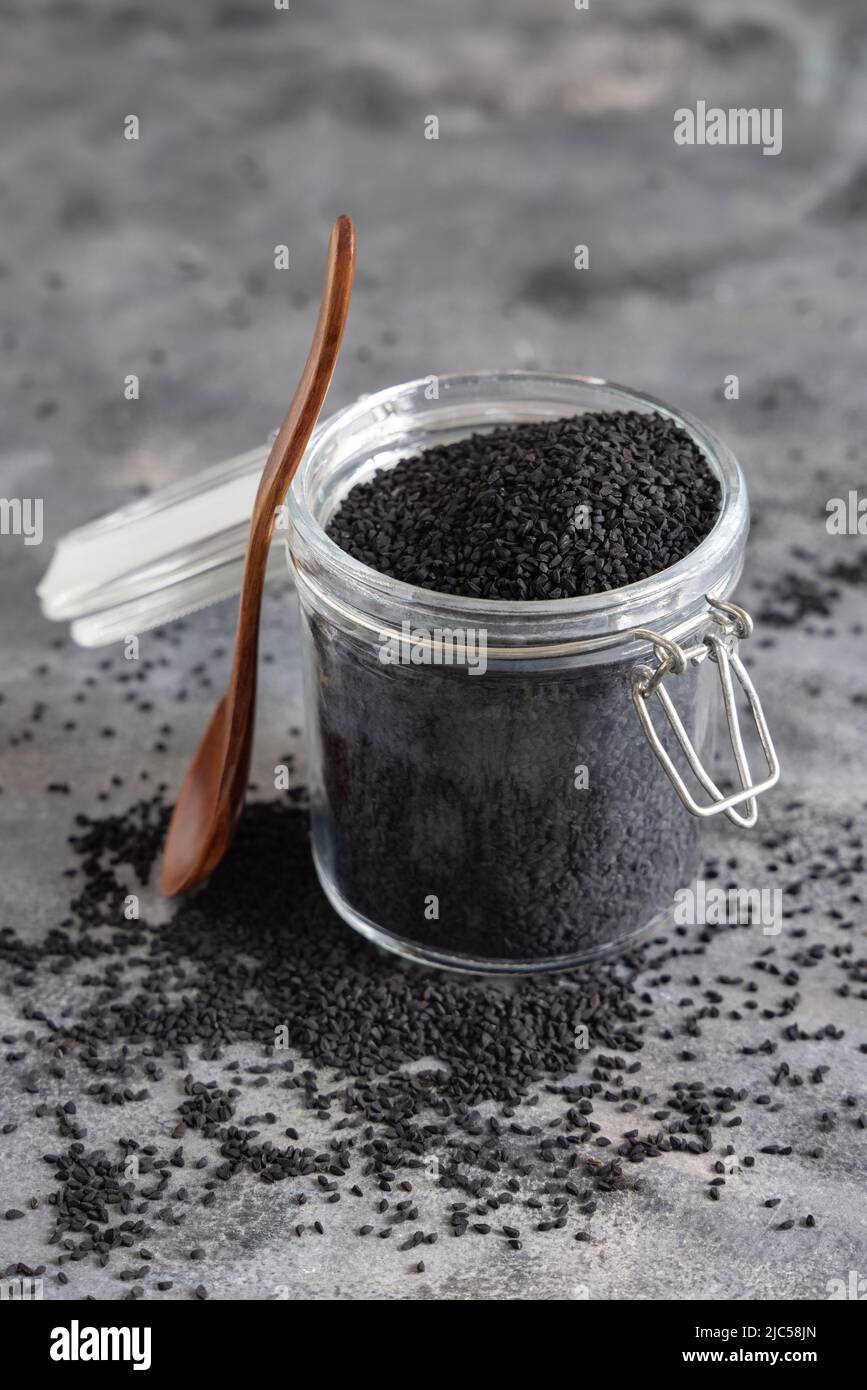 Indian spice Black cumin (nigella sativa or kalonji) seeds glass jar with a wooden spoon, close up. Traditional asian medicine, healthy and vegetarian Stock Photo