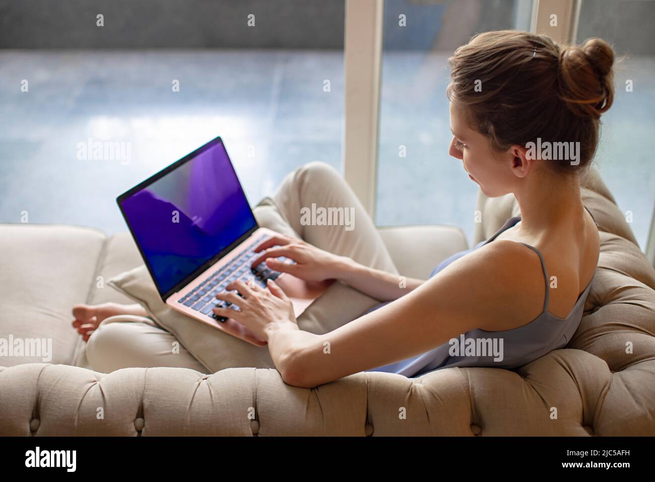 Young woman sitting on couch and working on a laptop Stock Photo