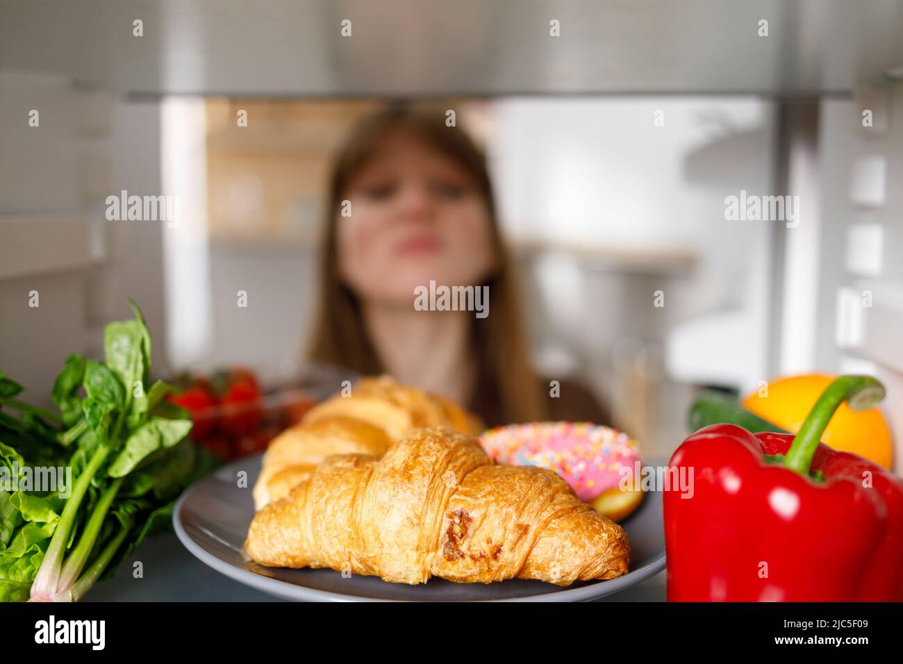 Selective focus of woman looking into fridge at the kitchen. Sweets and vegetables on the refrigerator shelf Stock Photo