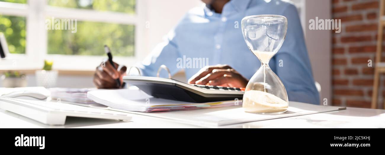 Hourglass In Front Of Businessperson Calculating Invoice Stock Photo