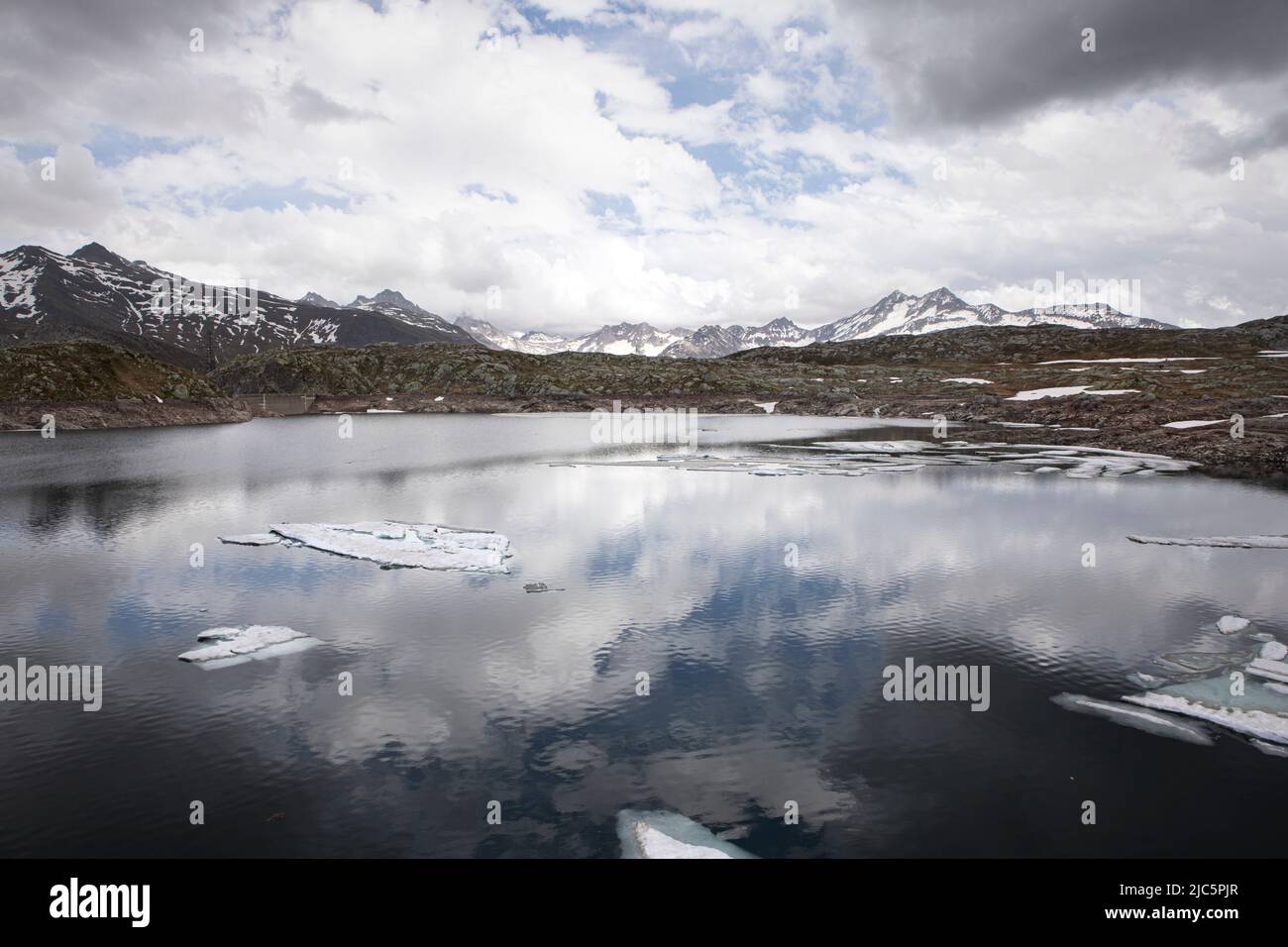 Totensee, view on cold lake in high alps mountains, cold, cloudy wether and atmospheric mood in high mountains, water surface with ice drifts. Grimsel Stock Photo