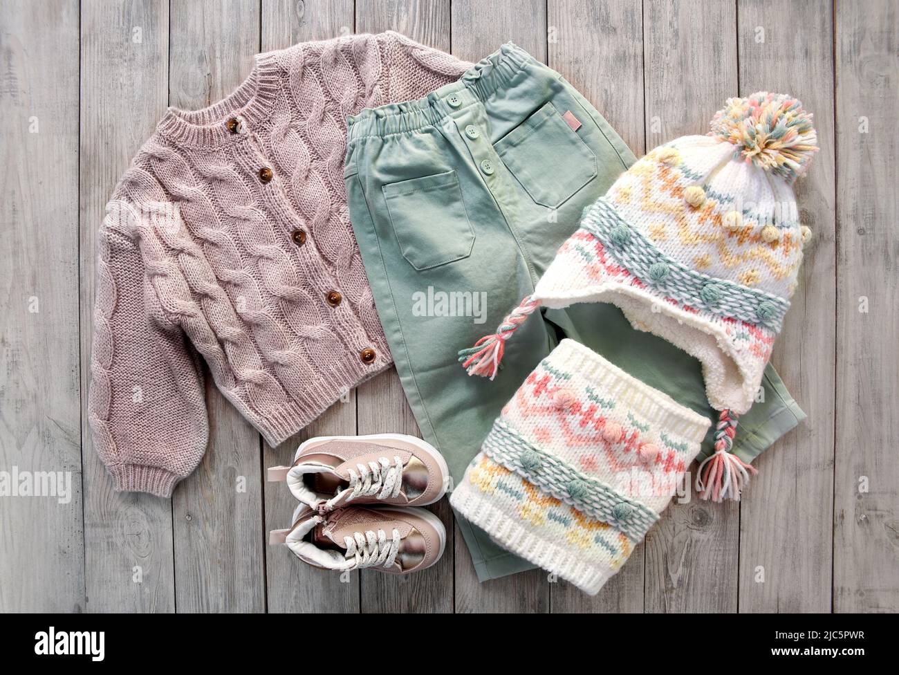 https://c8.alamy.com/comp/2JC5PWR/childs-girl-knitwear-set-on-wooden-background-flat-lay-kids-winter-woolen-clothes-top-view-toddler-knitted-cardiganpantshat-and-shoes-collectio-2JC5PWR.jpg