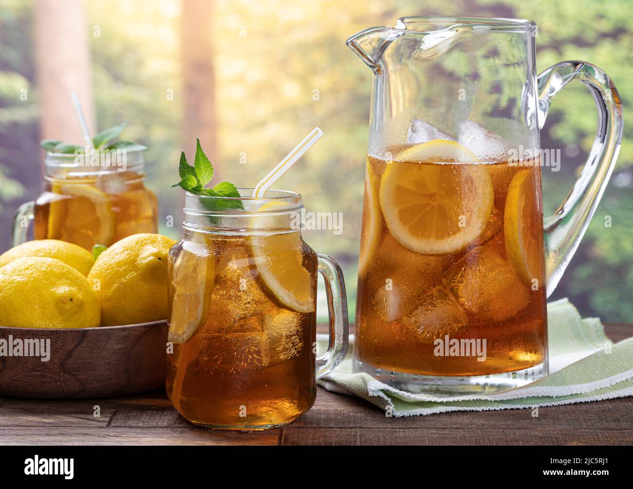 https://c8.alamy.com/comp/2JC5RJ1/glass-and-pitcher-of-iced-tea-with-mint-lemon-slices-and-ice-on-an-outdoor-wooden-table-with-rural-summer-background-2JC5RJ1.jpg