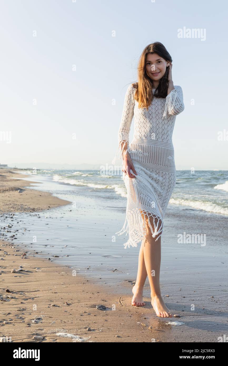 Pretty young woman looking at camera on beach with sea at background ...