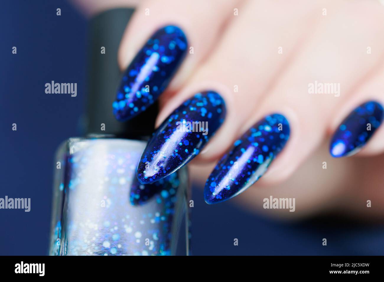 Female hand with long nails and a bottle of light blue color nail polish Stock Photo