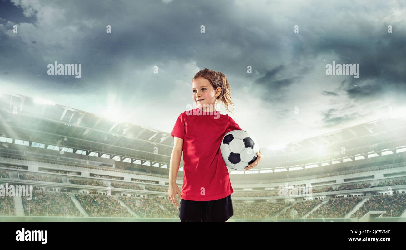 Portrait of little girl, football player in red uniform standing with