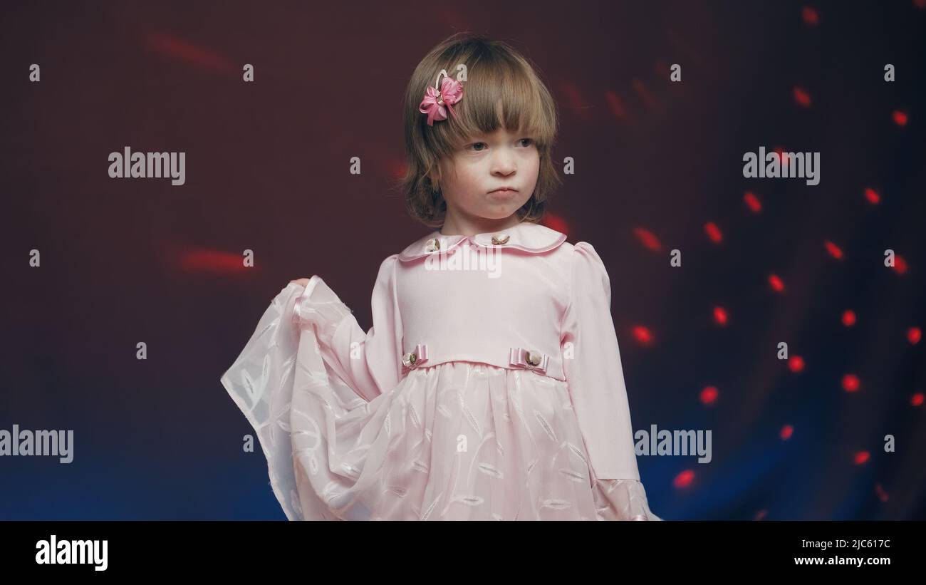 Cute little girl in a vintage pink dress stands on a dark background ...