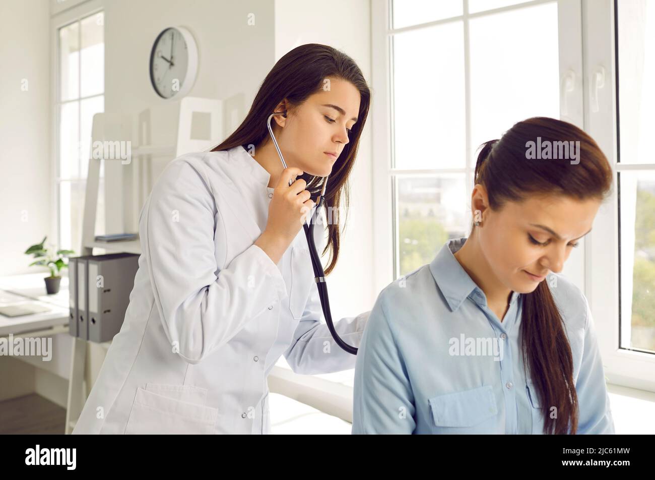Young female doctor checks woman's breathing and heartbeat at appointment at medical clinic