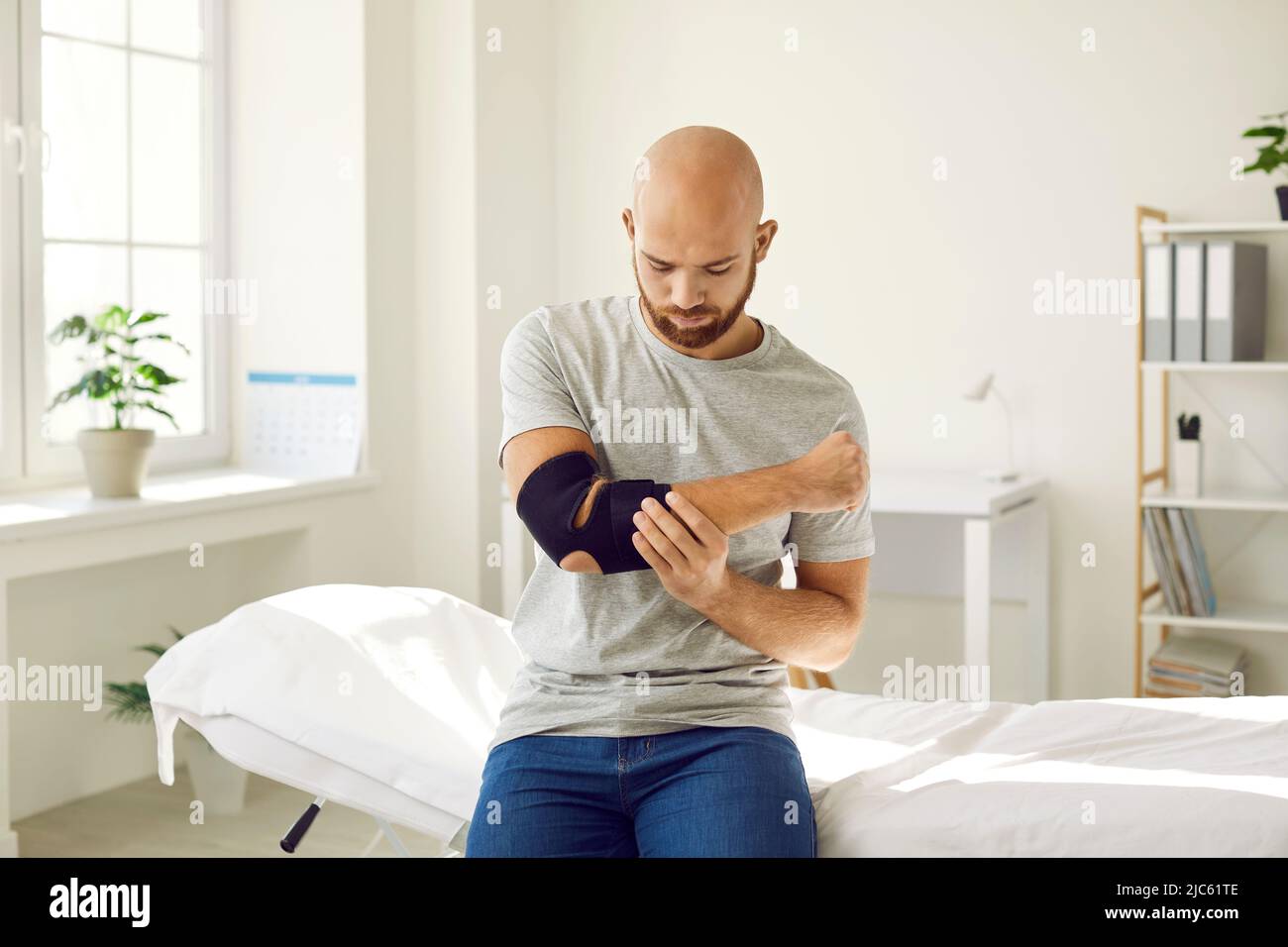 Man puts on bandage on injured elbow which serves to restore and relieve joint pain. Stock Photo