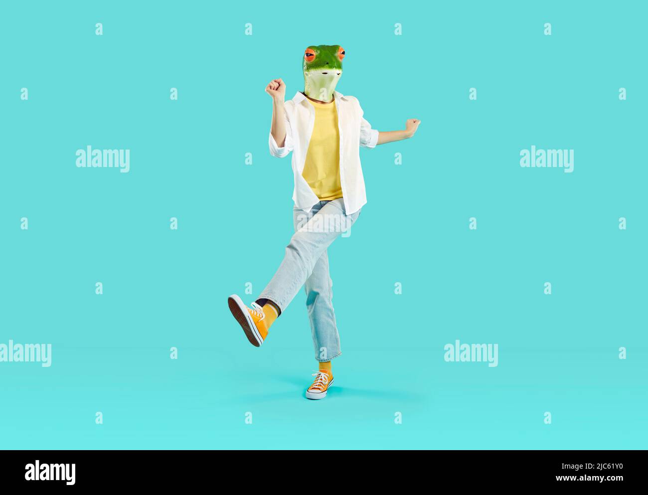 Strange woman in funny frog mask dancing and jumping isolated on turquoise background Stock Photo