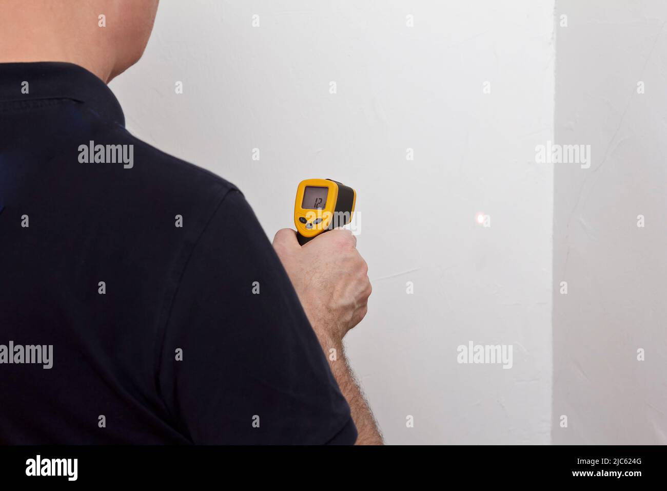 Save energy concept: man measuring the temperature of an external white wall with an infrared or laser thermometer. Stock Photo