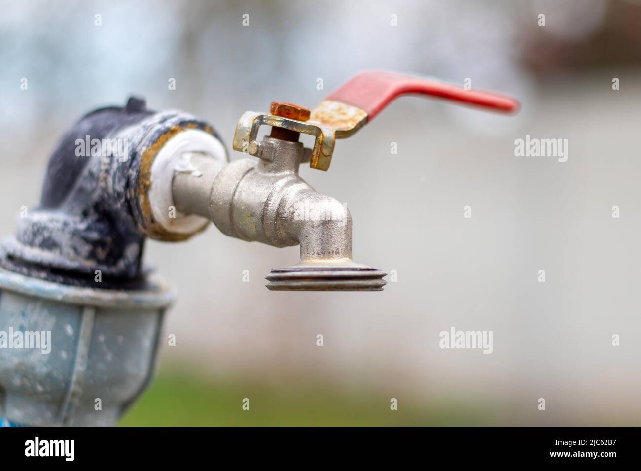 Water faucet on the background of nature. Opening or closing a faucet to save water indicates a water shortage problem. Rustic fountain with daylight. Stock Photo