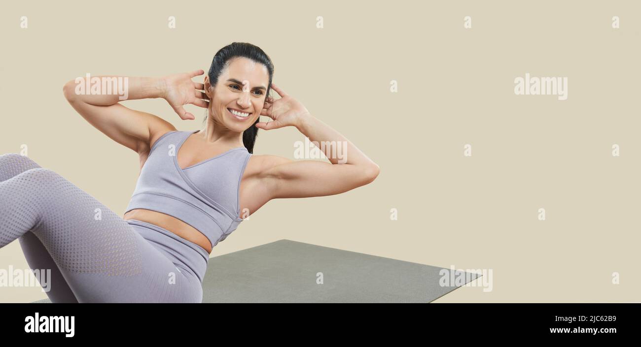 Young sporty woman practicing exercises for upper and lower abs isolated on beige background. Stock Photo