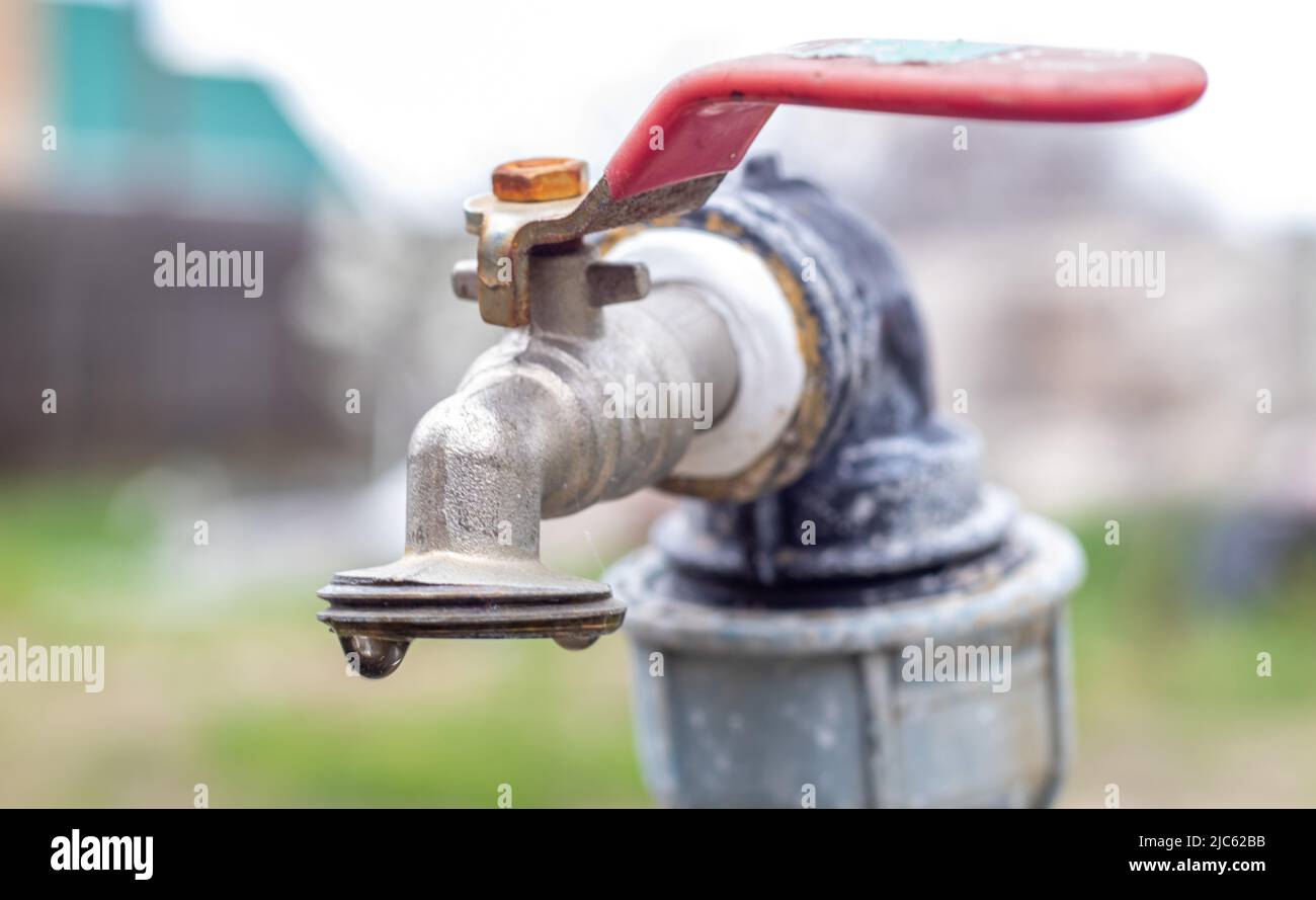 Water faucet on the background of nature. Opening or closing a faucet to save water indicates a water shortage problem. Rustic fountain with daylight. Stock Photo