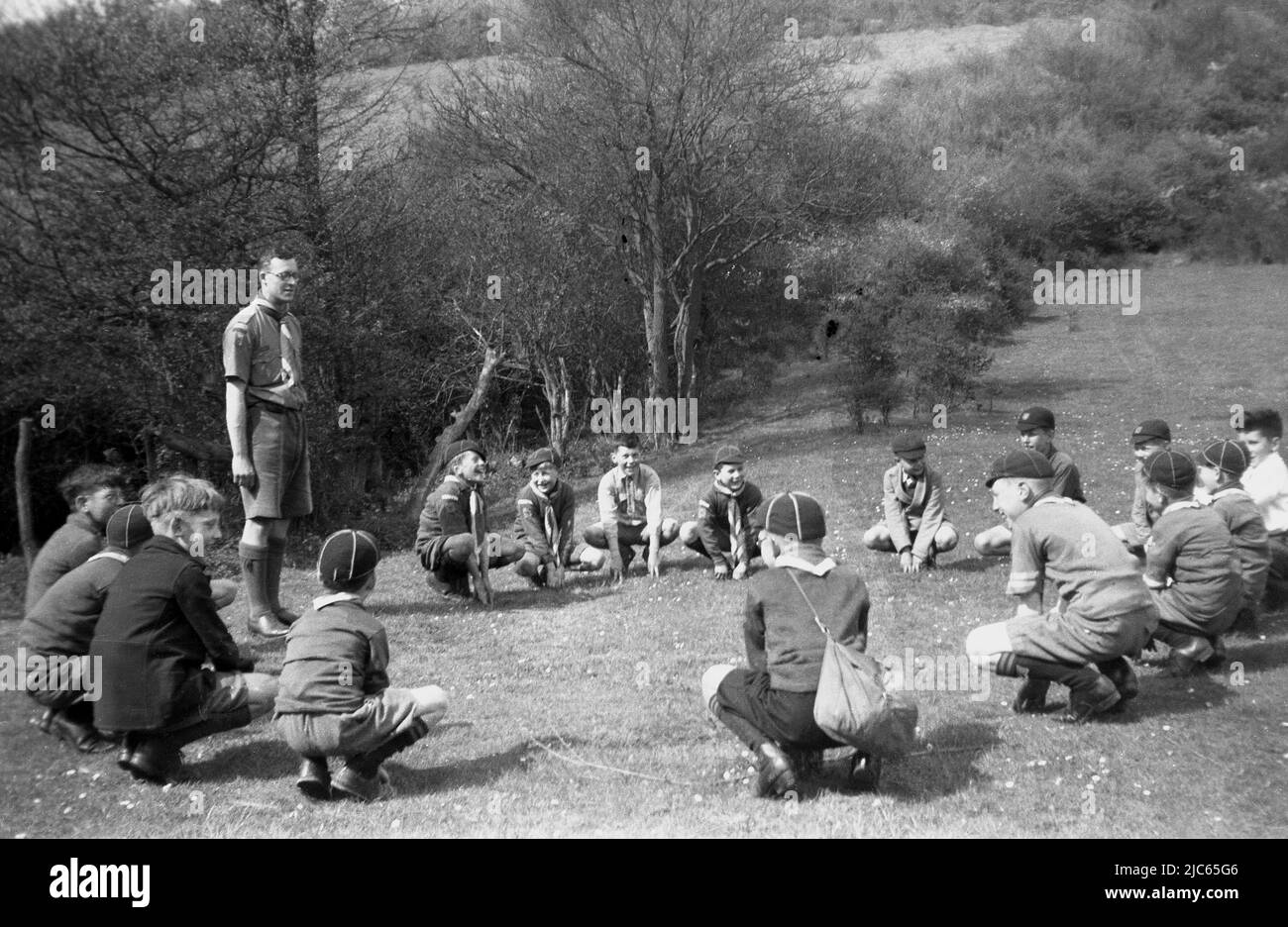 1939, a scout master with cub scouts, the 17th Coulsdon, doing the scouting ceremony of the Grand Howl at Devils Den Woods, Dorking, Surrey, England, UK. In this era, young boy or cub scouts  (8-10 year-olds) were known as Wolf Cubs. Devised by Robert Baden-Powell, the founder of the Scouting movement, the Grand Howl was based on The Jungle Book', a novel by Rudyard Kipling, where describes a wolf pack meeting, which begins with everyone circling their leader and howling. In scouting, this became the 'Grand Howl', with the idea being that the young scouts gather together and focus. Stock Photo