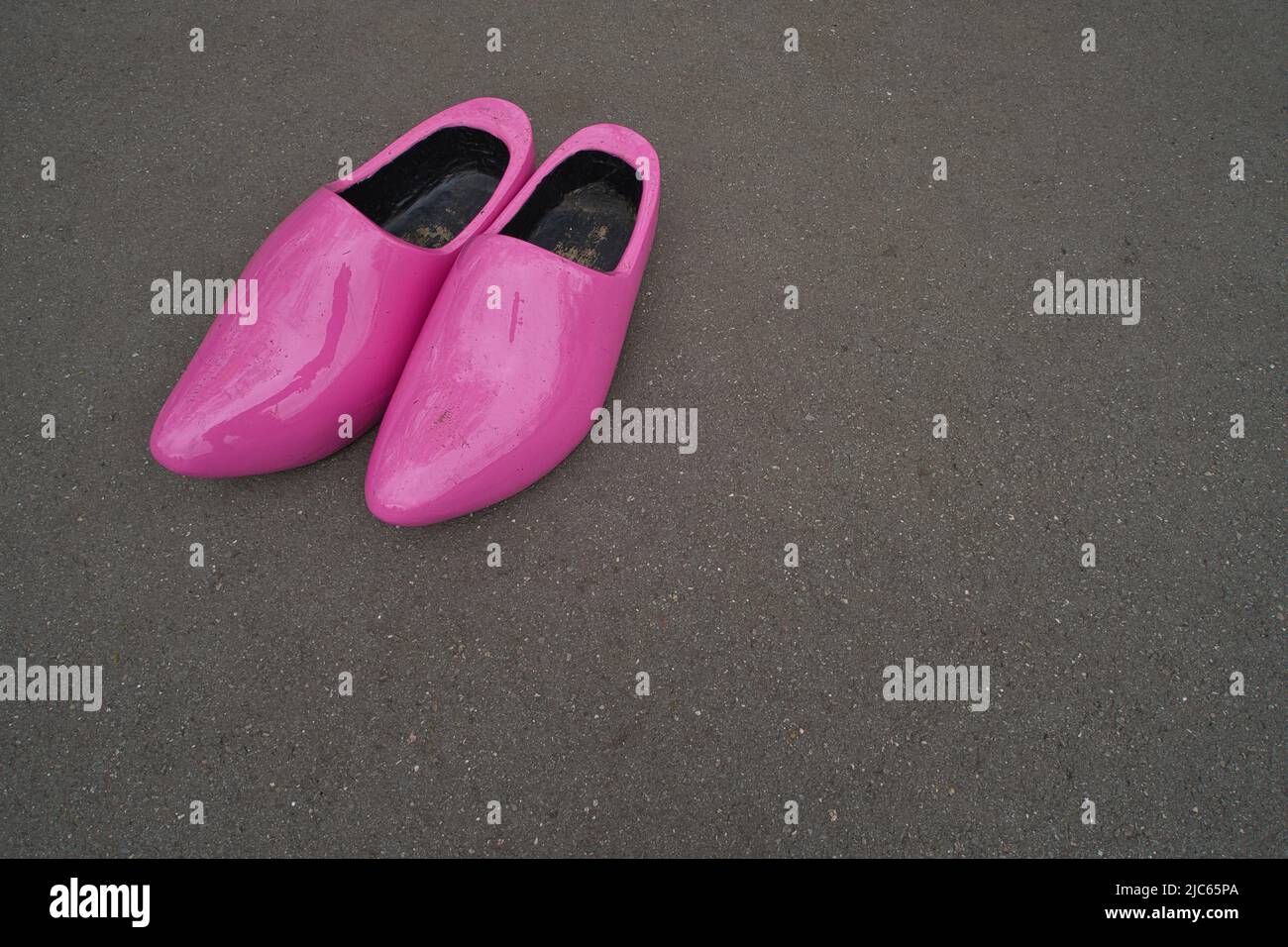 A pair of pink lacquered wooden shoes or clogs on the gray asphalt Stock Photo