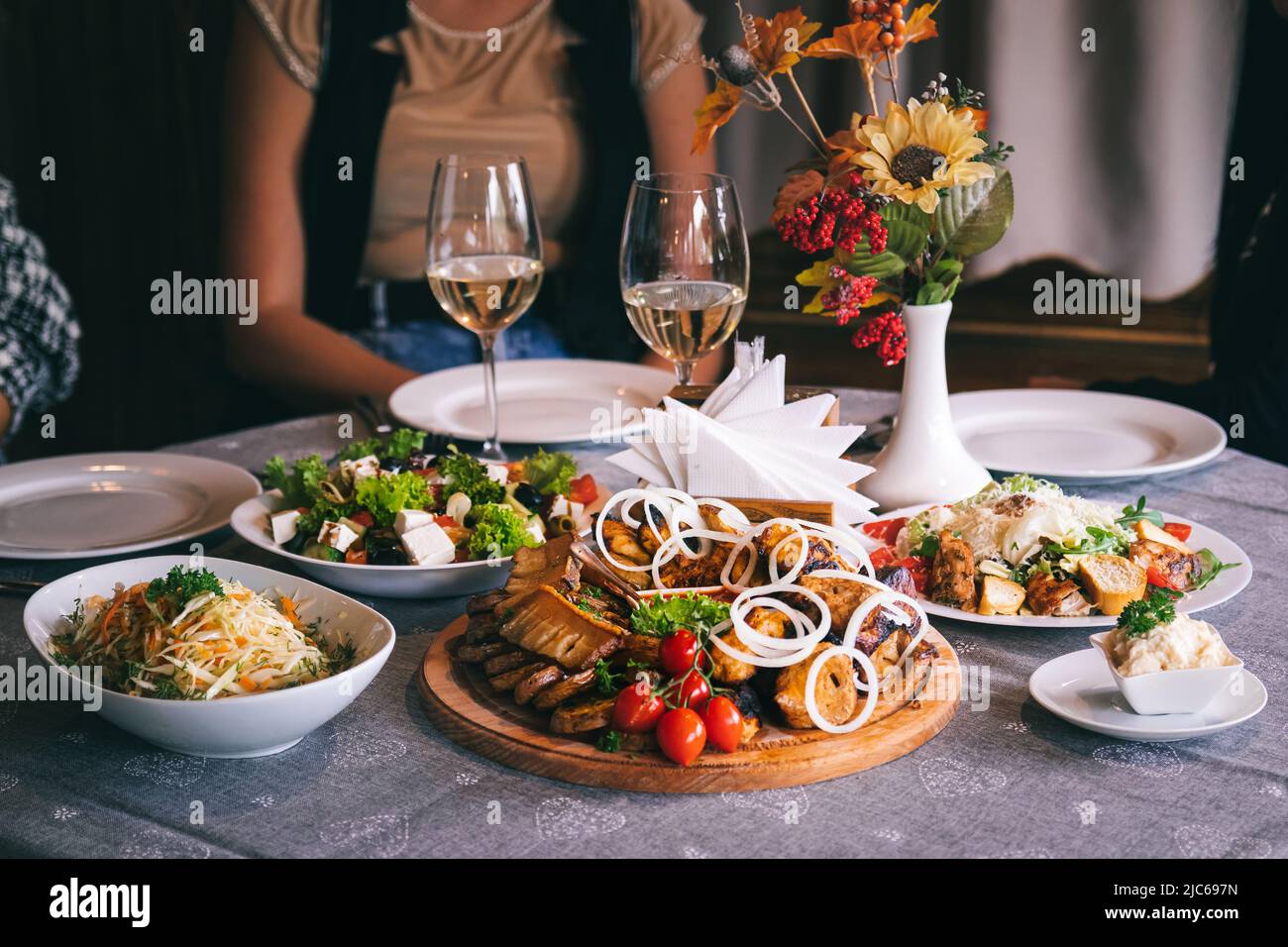 Plate with barbecue, sauce and salads. Dinner at the restaurant. In the background are glasses of white wine. Stock Photo