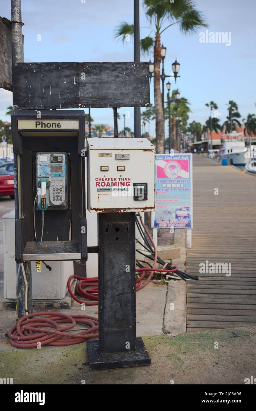 ORANJESTAD, ARUBA - DECEMBER 3, 2021: Old public phone and a box from Bells Technologies stating Cheaper Than Roaming, located along pier Stock Photo