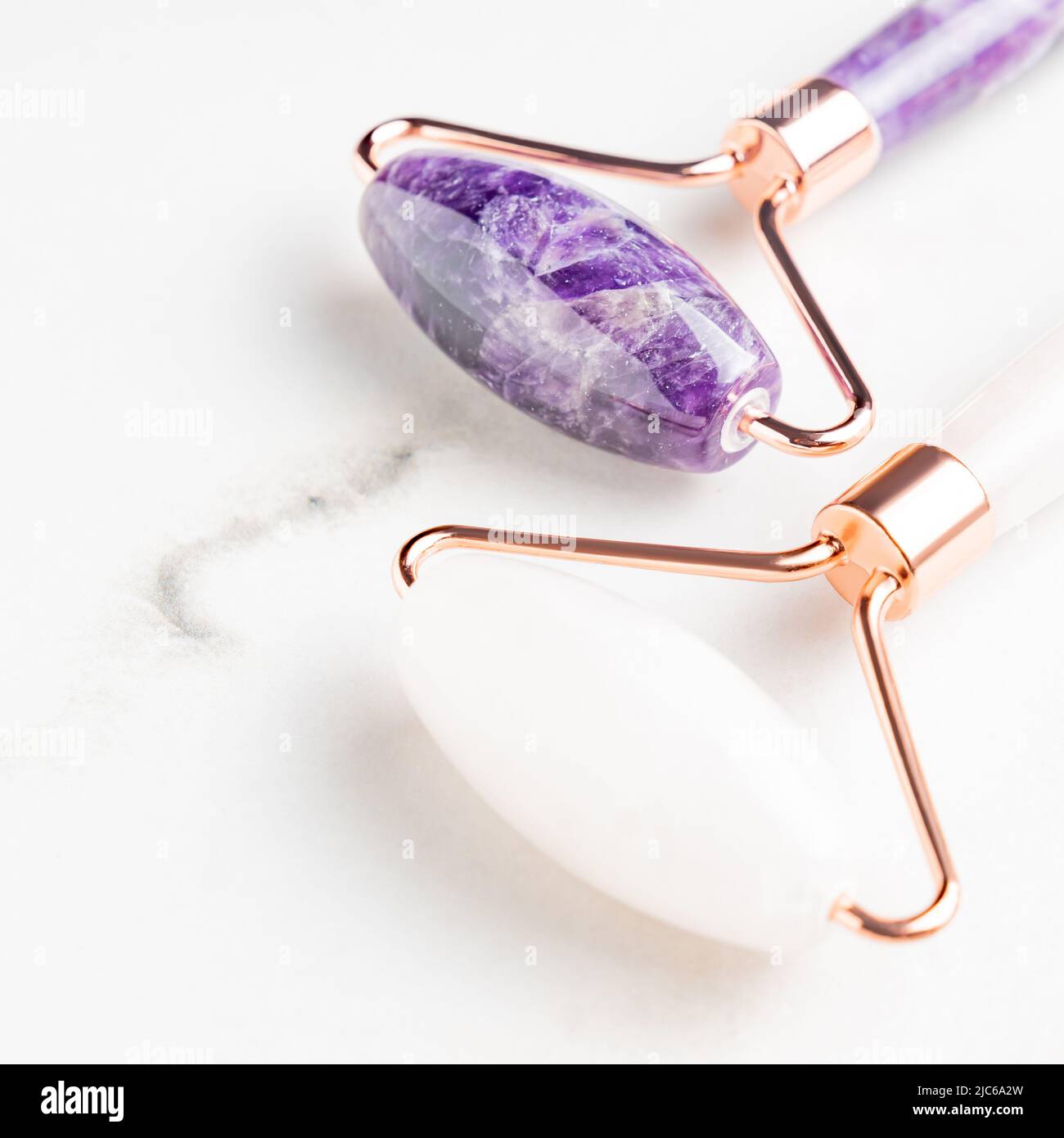 Set of Facial massage amethyst gua sha rollers on white marble background. Face roller, massager