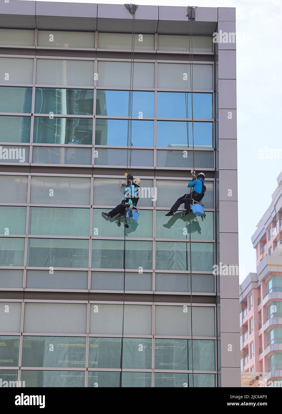 high rise building Window washers cleaning the glass facade of a modern building, skyscraper high risk work. Stock Photo