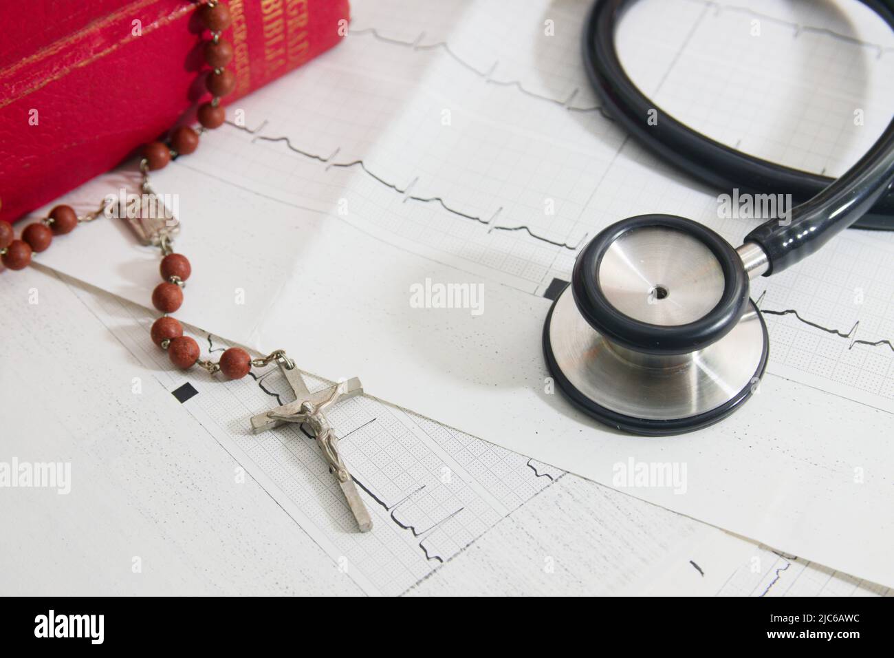 Close-up of a crucifix and a stethoscope on a patient's printed cardiograms next to a bible Stock Photo