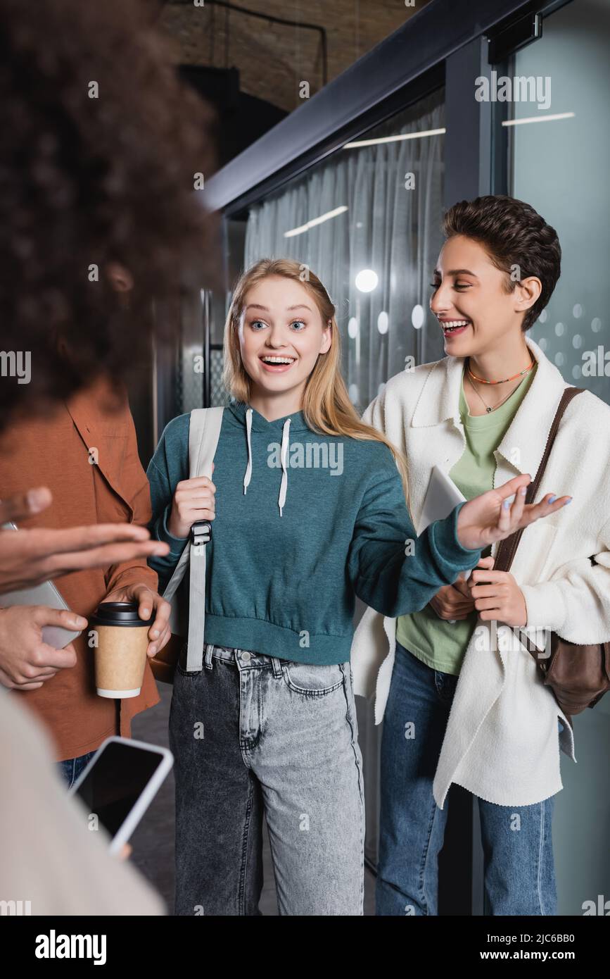 smiling woman pointing with hand while talking to multicultural students in university Stock Photo