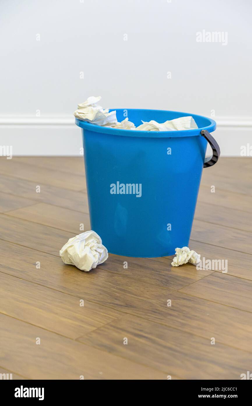 a blue plastic bucket filled with used tissues sits on a wooden floor ...