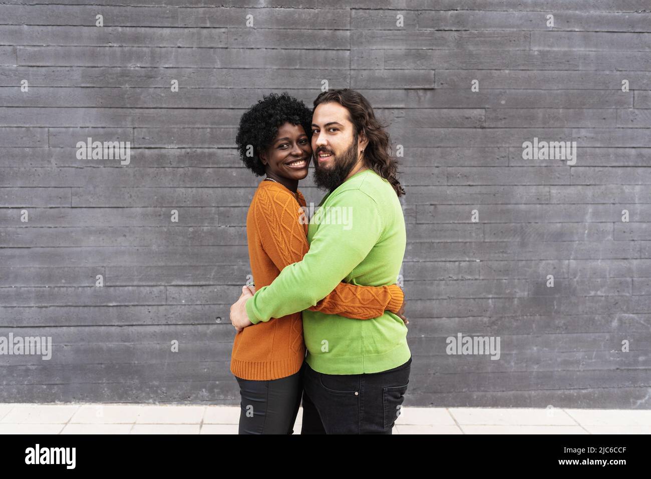 Interracial couple smiling while hugging each other outdoors. Stock Photo