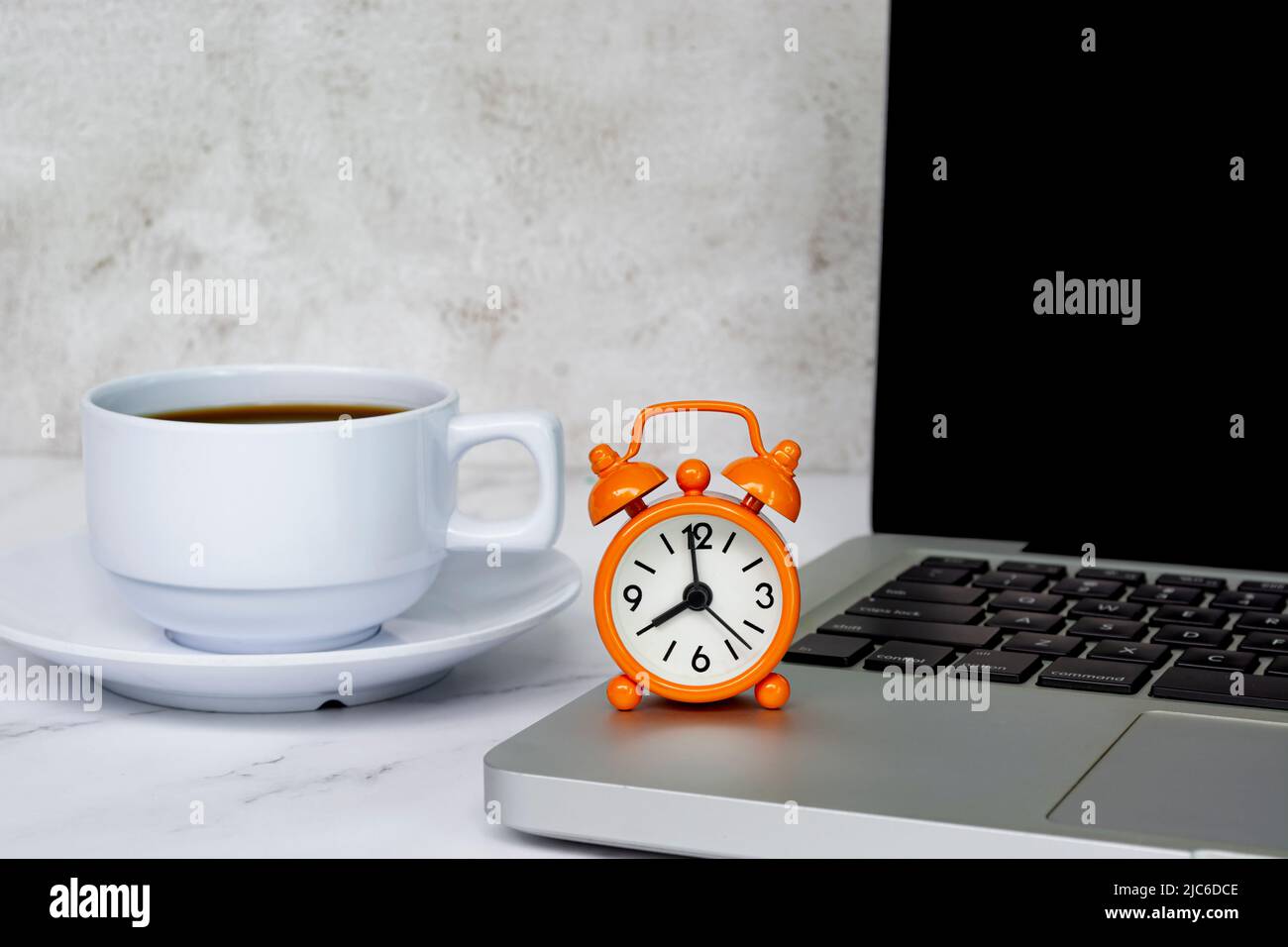 Alarm clock on laptop or notebook with coffee cup on a table. The clock