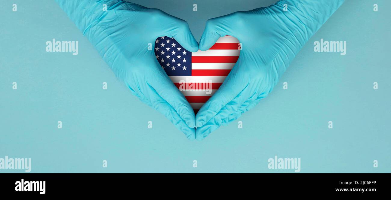 Doctors hands wearing blue surgical gloves making hear shape symbol with USA flag Stock Photo