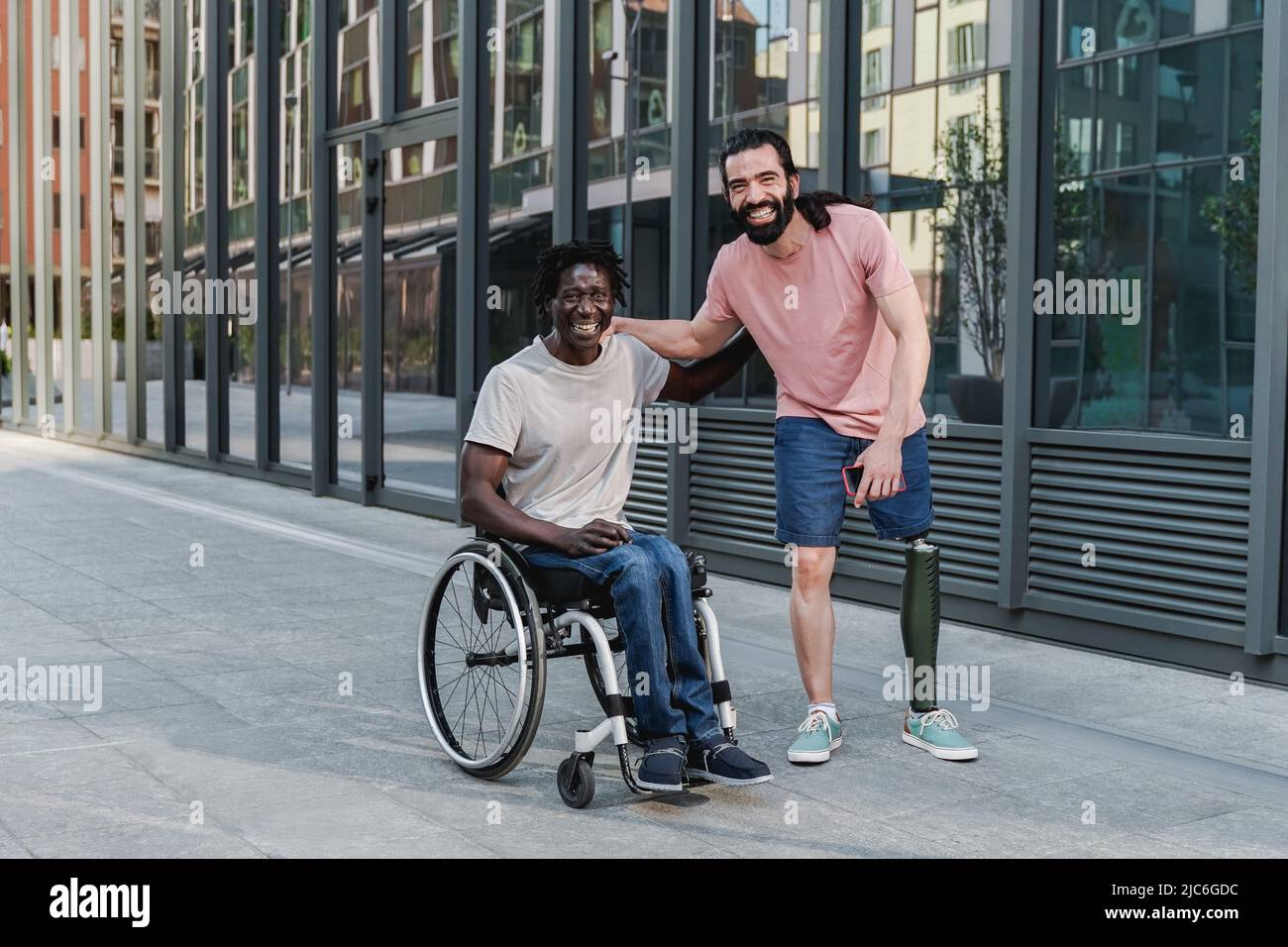 Multiracial friends with disability having fun looking at camera outdoor - Focus on African man sitting on wheelchair Stock Photo