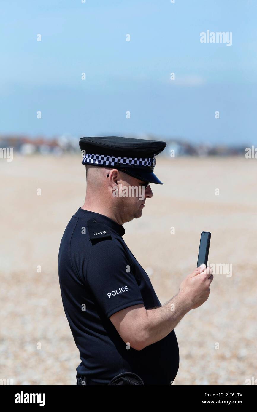 England, Kent, Dungeness, Police officer using his phone to video a beach landing of refugeees. Stock Photo