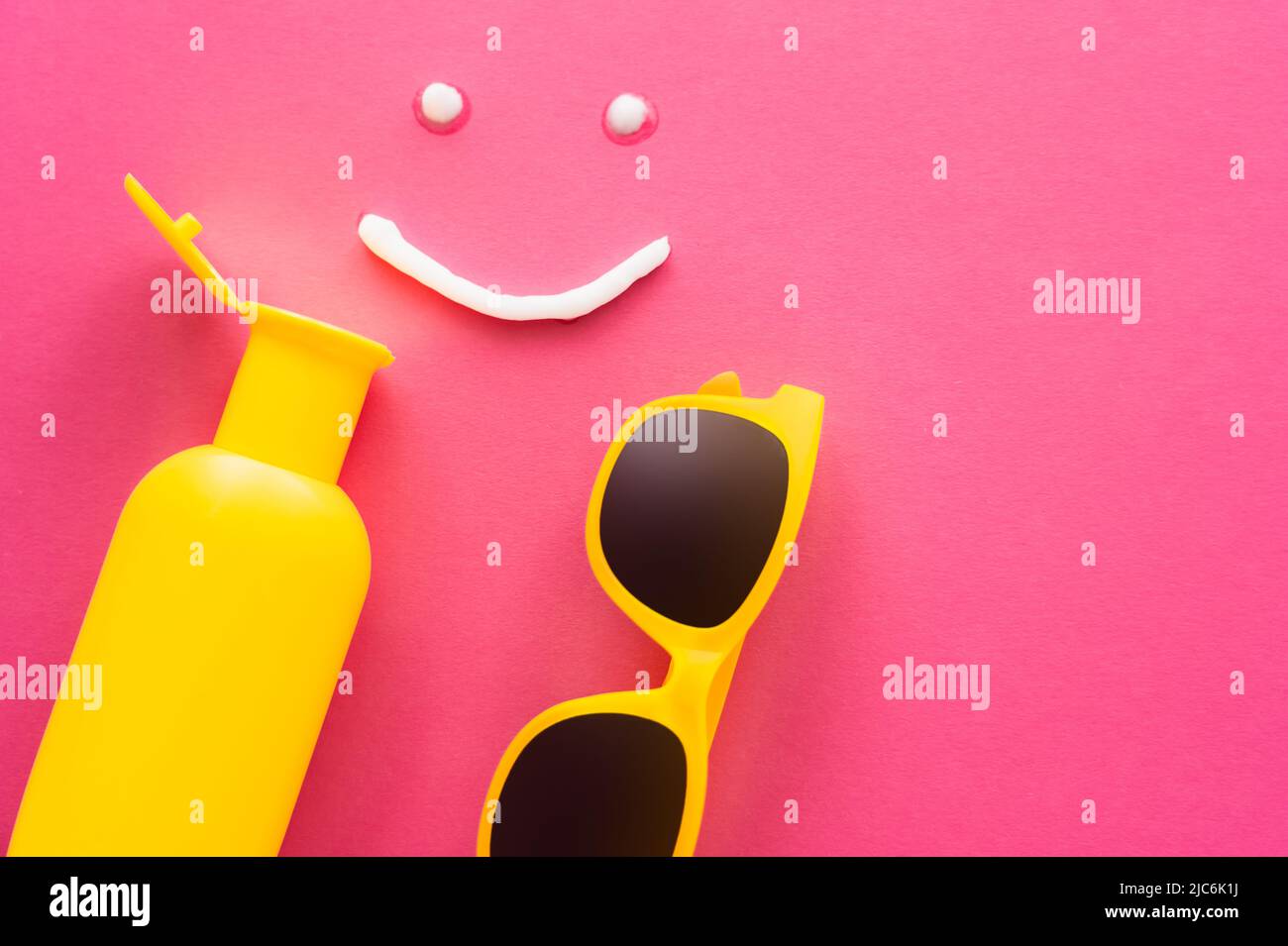 Top view of sunglasses near smile sign and sunscreen on pink background Stock Photo