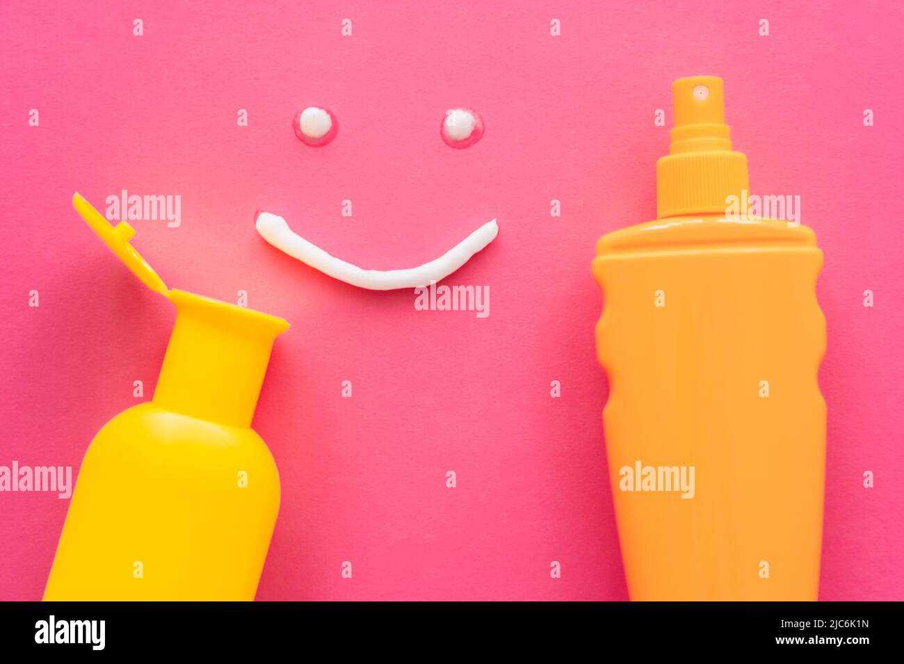 Top view of smile sign near bottles of sunscreens on pink background Stock Photo