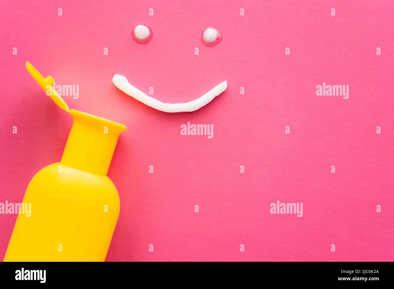 Top view of sunscreen near smile sign on pink background Stock Photo