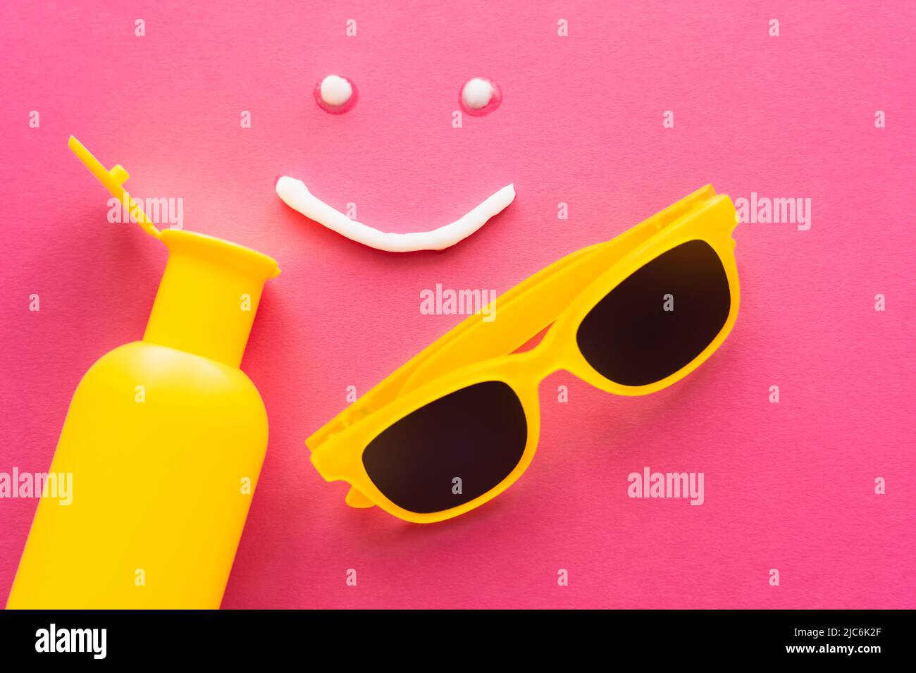 Top view of smile sign from sunscreen near bottle and sunglasses on pink background Stock Photo