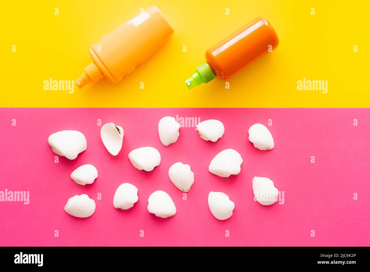 Top view of seashells near bottles of sunscreens on yellow and pink background Stock Photo
