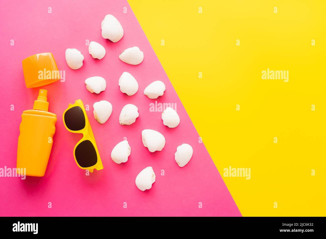 Top view of sunblock near sunglasses and seashells on pink and yellow background Stock Photo