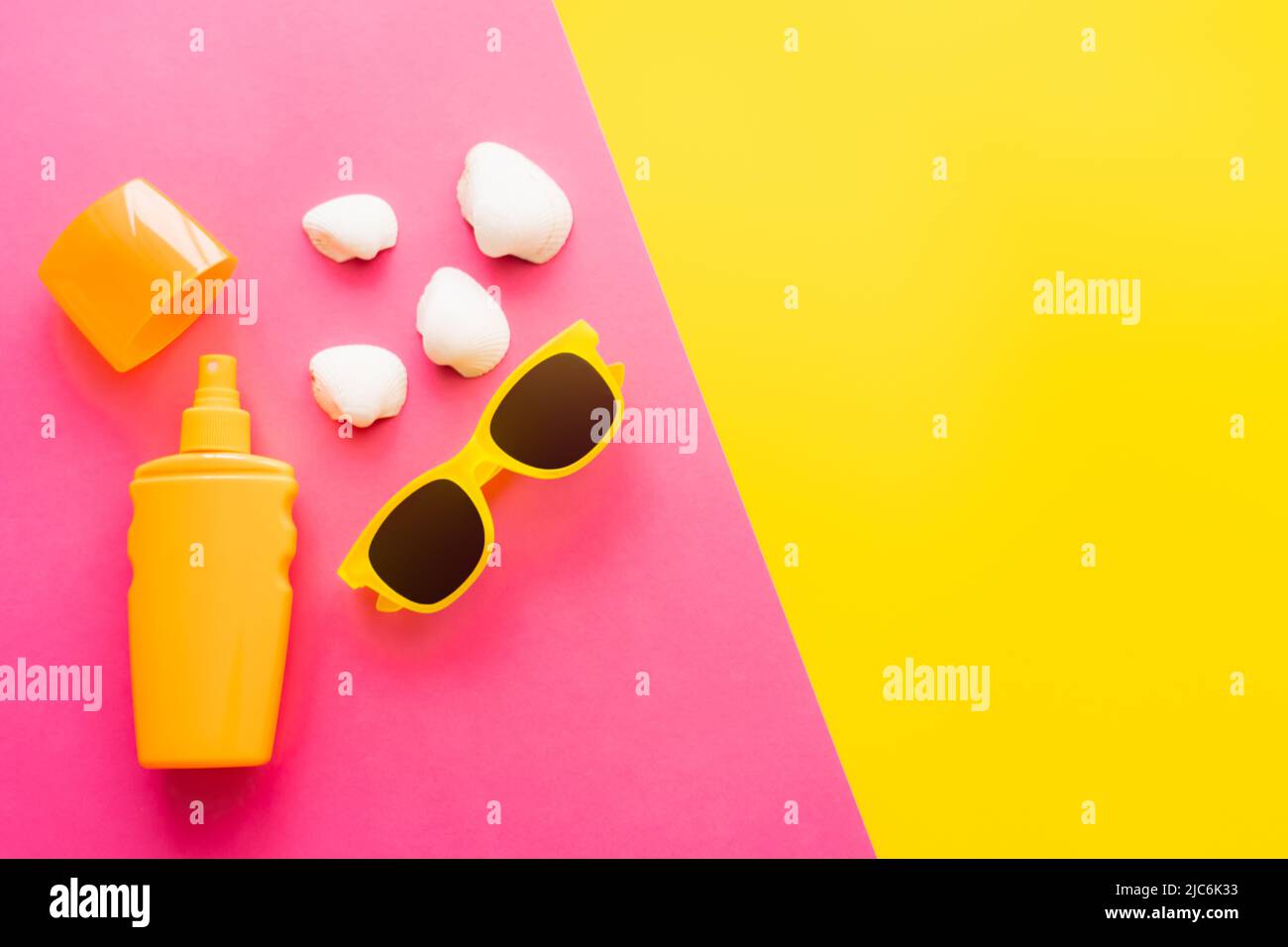 Top view of sunblock and sunglasses near seashells on pink and yellow background Stock Photo